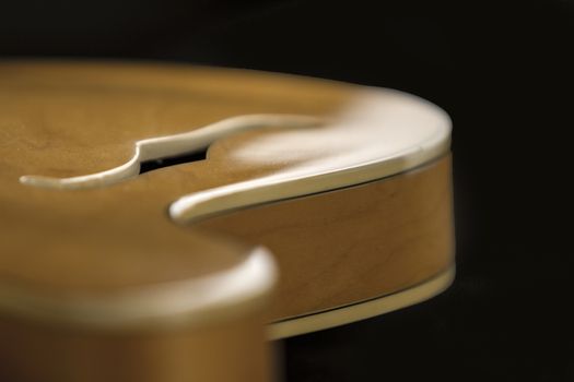 Vintage archtop guitar in natural maple close-up high angle view with F-hole detail in selective focus and black background