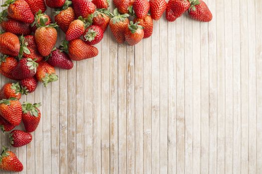 Strawberries copy space with strawberries in the upper left corner scattered on a wooden background taken from above