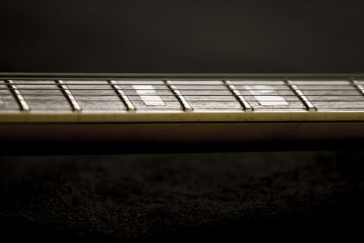 Vintage archtop guitar in natural maple close-up high angle view on black background, rosewood fingerboard with frets and fret markers detail in selective focus