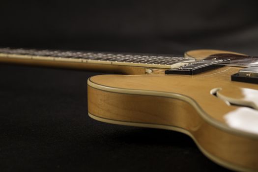 Vintage archtop guitar in natural maple close-up high angle side view in selective focus on black background