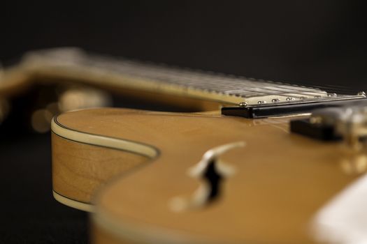 Vintage archtop guitar in natural maple close-up high angle view on black background, pick-up side in selective focus
