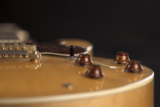 Vintage archtop guitar in natural maple close-up high angle view on black background, golden bridge, volume and tone controls detail in selective focus