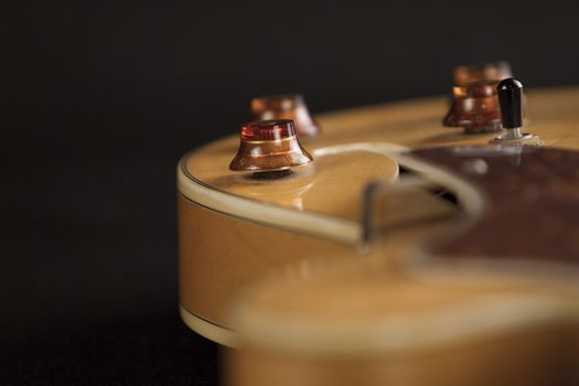 Vintage archtop guitar in natural maple close-up high angle view on black background, controls detail in selective focus