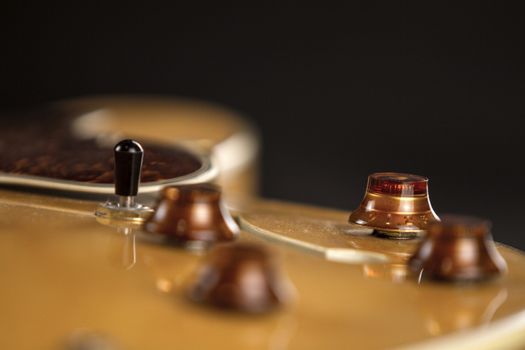 Vintage archtop guitar in natural maple close-up high angle view on black background, golden bridge, volume and tone controls detail in selective focus