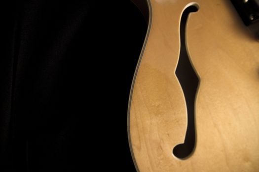Vintage archtop guitar in natural maple close-up from above on black background, F-hole detail