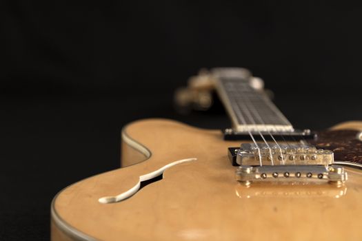 Vintage archtop guitar in natural maple close-up high angle view on black background, bridge and F-hole detail in selective focus