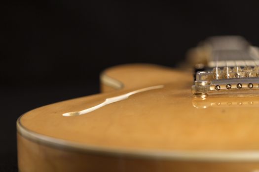 Vintage archtop guitar in natural maple close-up high angle view on black background, golden hardware detail in selective focus