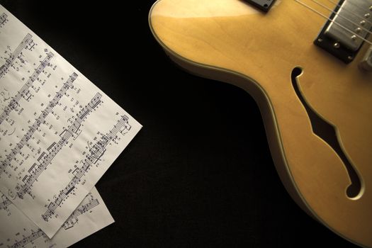 Vintage archtop guitar in natural maple close-up from above with musci sheets on black background