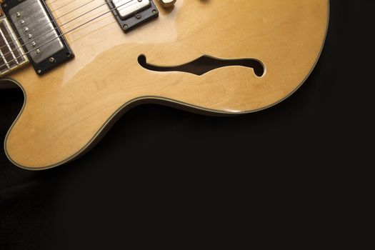 Vintage archtop guitar in natural maple close-up from above on black background, F-hole detail