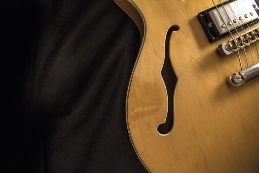 Vintage archtop guitar in natural maple close-up from above on black background, F-hole detail