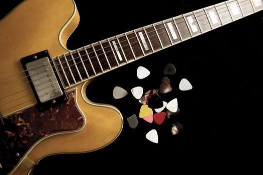 Vintage archtop guitar in natural maple close-up from above on black background with various picks