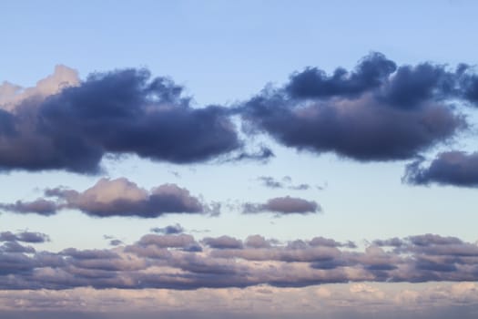 Impressive sky at sunset with layers of clouds tinged with pink that slope down towards the horizon