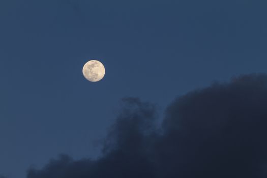 Full moon just risen in the dark blue sky with some gray clouds