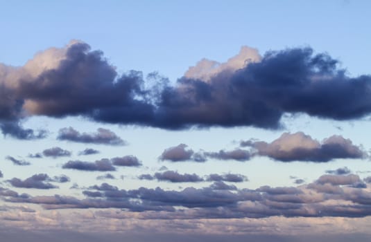 Impressive sky at sunset with layers of clouds tinged with pink that slope down towards the horizon