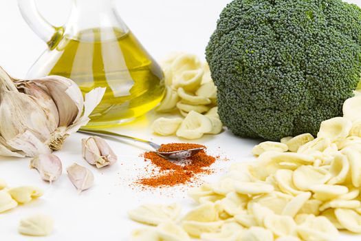 Close-up o f ingredients of typical italian recipe orecchiette ai broccoli: handmade durum wheat flour pasta orecchiette, broccoli, extra virgin olive oil, garlic and ground chili on white background