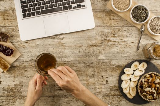 The habits of modern times: a woman shot from above on a wooden table, makes a healthy and vegan breakfast, but in front of the open laptop