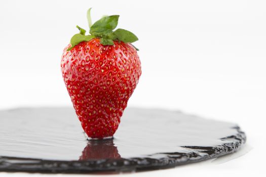 Close-up of a strawberries isolated on a wet round slate plate on a white background shot in high angle view with selective focus