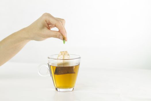 Closeup of a woman hand dipping a tea bag in a glass cup full of water with beautiful red-colored effects in the transparency of the water