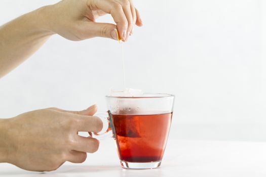 Close-up of a woman hand dipping a sachet of Hibiscus Tea in a glass cup full of water with beautiful red-colored effects in the transparency of water