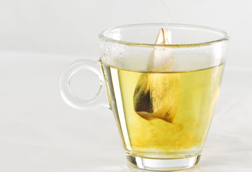 Closeup of a tea bag in a glass cup full of water with beautiful yellow color effects in the transparency of the water