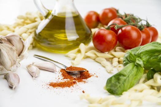 Close-up of italian typical pasta recipe: handmade durum wheat flour pasta, tomatoes, garlic, extra virgin olive oil, ground chili, parsley and basil on white background