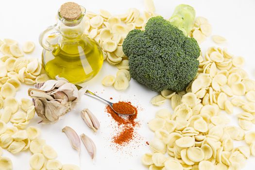 Close-up o f ingredients of typical italian recipe orecchiette ai broccoli: handmade durum wheat flour pasta orecchiette, broccoli, extra virgin olive oil, garlic and ground chili on white background