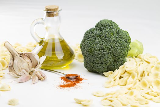 Close-up o f ingredients of typical italian recipe orecchiette ai broccoli: handmade durum wheat flour pasta orecchiette, broccoli, extra virgin olive oil, garlic and ground chili on white background