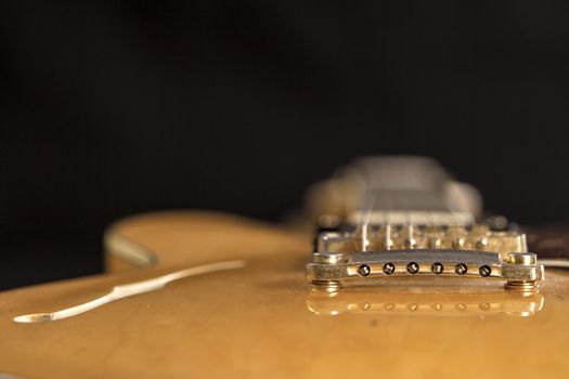 Vintage archtop guitar in natural maple close-up high angle view on black background, golden hardware detail in selective focus