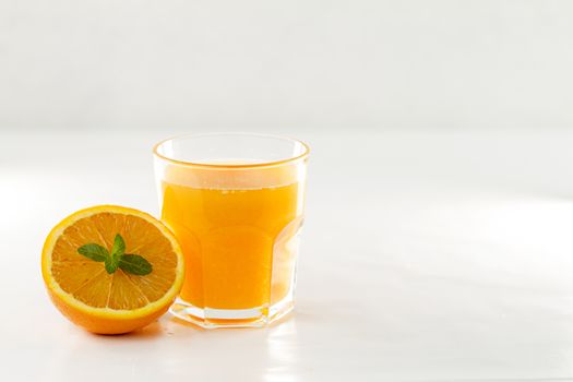 An inviting glass full of orange juice and a half one with a fresh mint leaf in its center on a white background