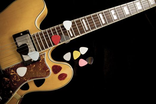 Vintage archtop guitar in natural maple close-up from above on black background with various picks