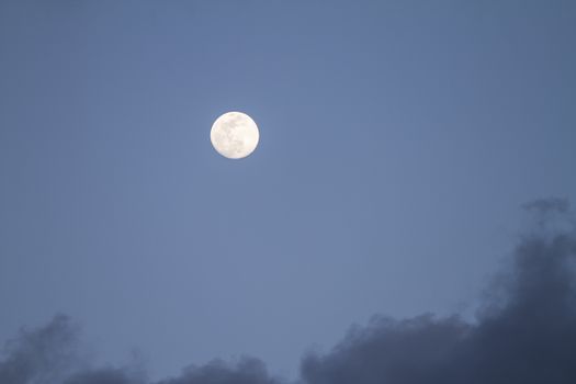 Full moon just risen in the dark blue sky with some gray clouds