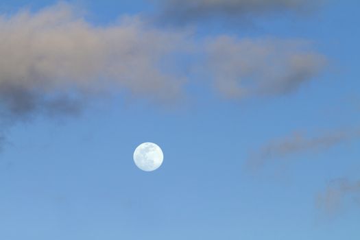 Full moon in twilight time in the clear blue sky with some light gray clouds