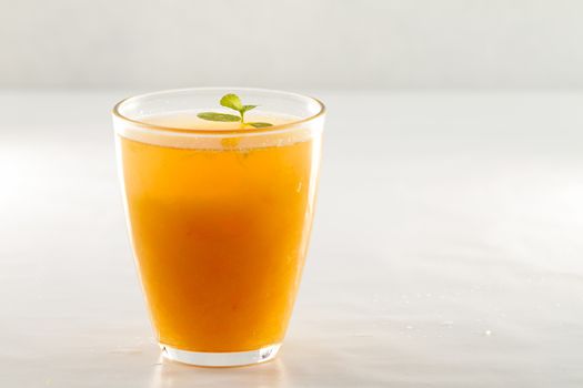 An inviting glass full of orange juice with a fresh mint leaf that floats on white white background