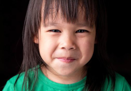 Portrait face of Asian little child girl with happy expression on dark background.