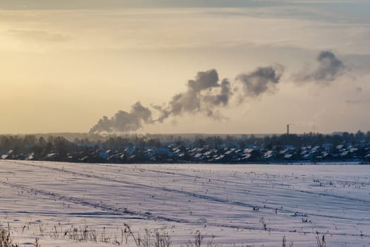 Snowy field on a frosty winter day and a city with smoke from pipes on the horizon