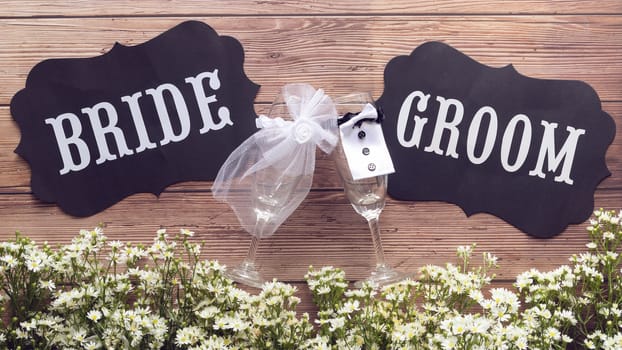 champagne glass in wedding dress with Bride and Groom text sign on wooden background decorated with tiny white flower, vintage style. wedding sign concept