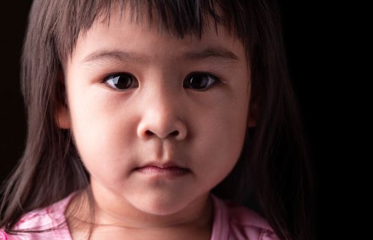Portrait face of Asian little child girl with confidence expression on dark background.