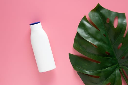 cosmetic nature skincare concept. white cosmetic bottle container with blank label for branding mock up, decorate with green tropical leaves on pink background with copy space