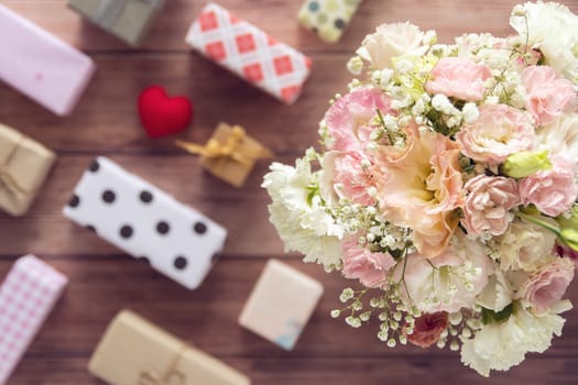 flat Lay of bouquet of beautiful romantic fresh flower with colorful gift box present on wooden background, top view