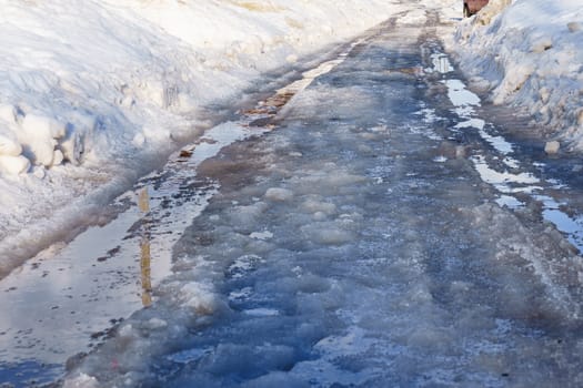 winter road covered with snow and ice with puddles and ruts, sunny day