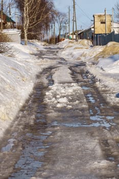 winter road covered with snow and ice with puddles and ruts, vertical shot