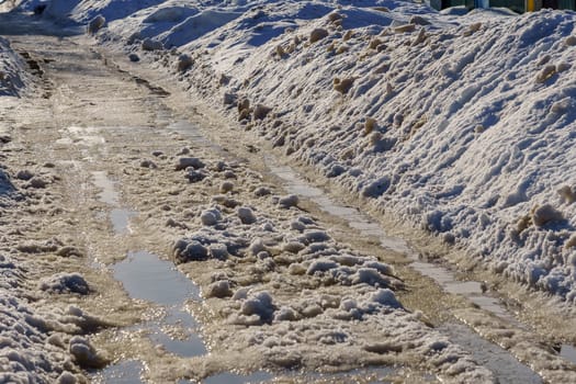 winter road covered with snow and ice with puddles and ruts, sunny day