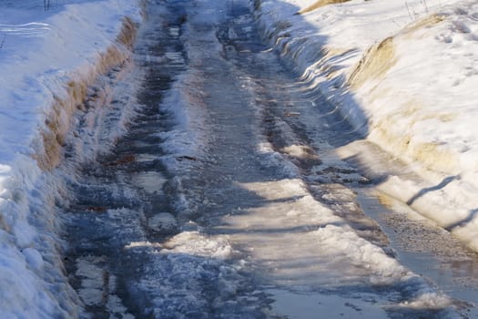 winter road covered with snow and ice with puddles and ruts, sunny day