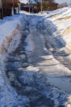 winter road covered with snow and ice with puddles and ruts, vertical shot