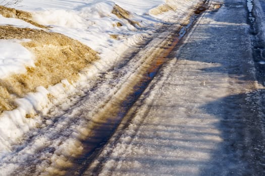 winter road covered with snow and ice with puddles and ruts, sunny day