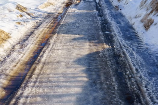 winter road covered with snow and ice with puddles and ruts, sunny day