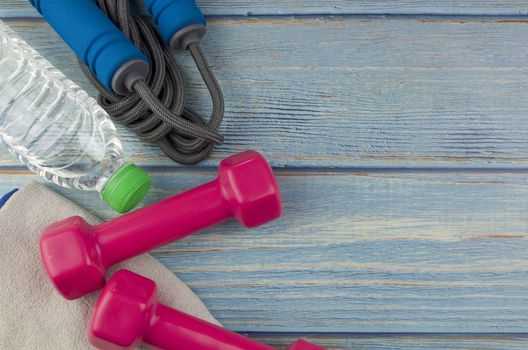 Top or flat lay view of dumbbells, towel, water and skipping rope with copy space area on blue wooden background. Healthy concept. Selective focus.