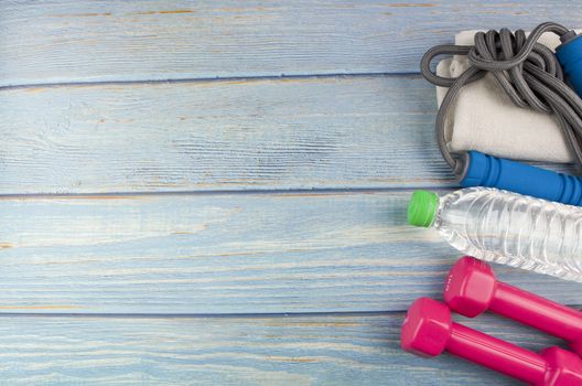 Top or flat lay view of dumbbells, towel, water and skipping rope with copy space area on blue wooden background. Healthy concept. Selective focus.