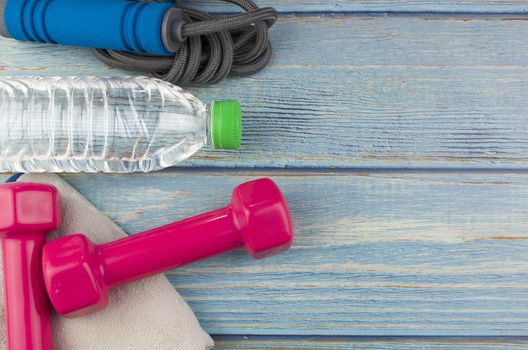 Top or flat lay view of dumbbells, towel, water and skipping rope with copy space area on blue wooden background. Healthy concept. Selective focus.