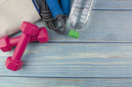 Top or flat lay view of dumbbells, towel, water and skipping rope with copy space area on blue wooden background. Healthy concept. Selective focus.